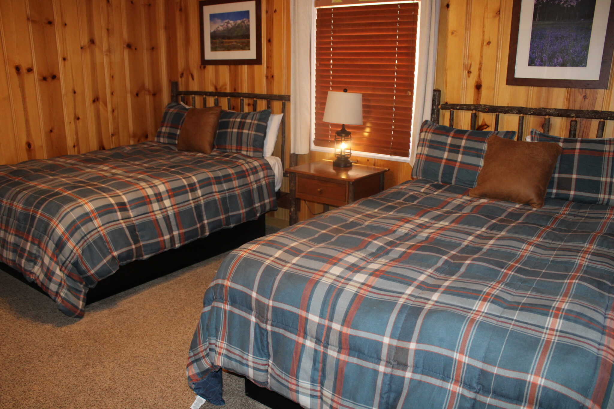A cozy room with two twin beds, wood paneling, and a window with blinds.
